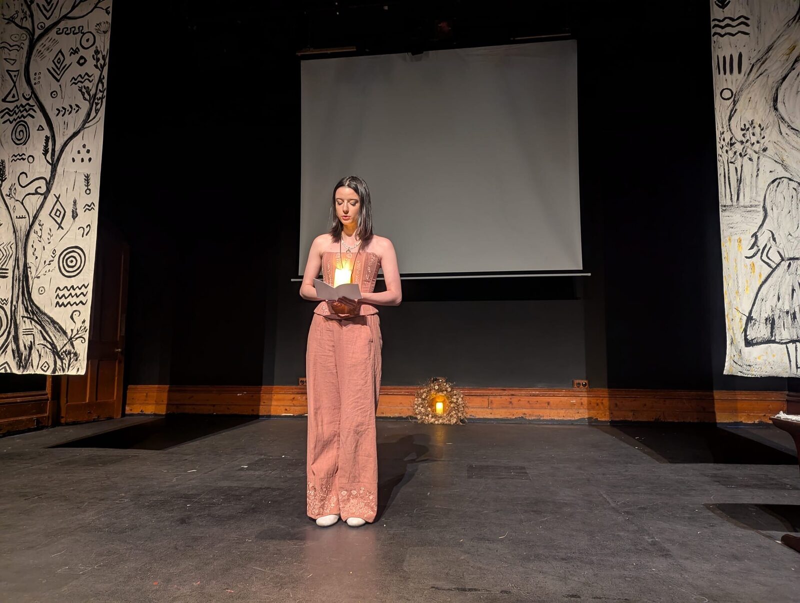 A lone performer stands centre stage holding a candle, framed by hand-painted banners of Trypillian symbols.